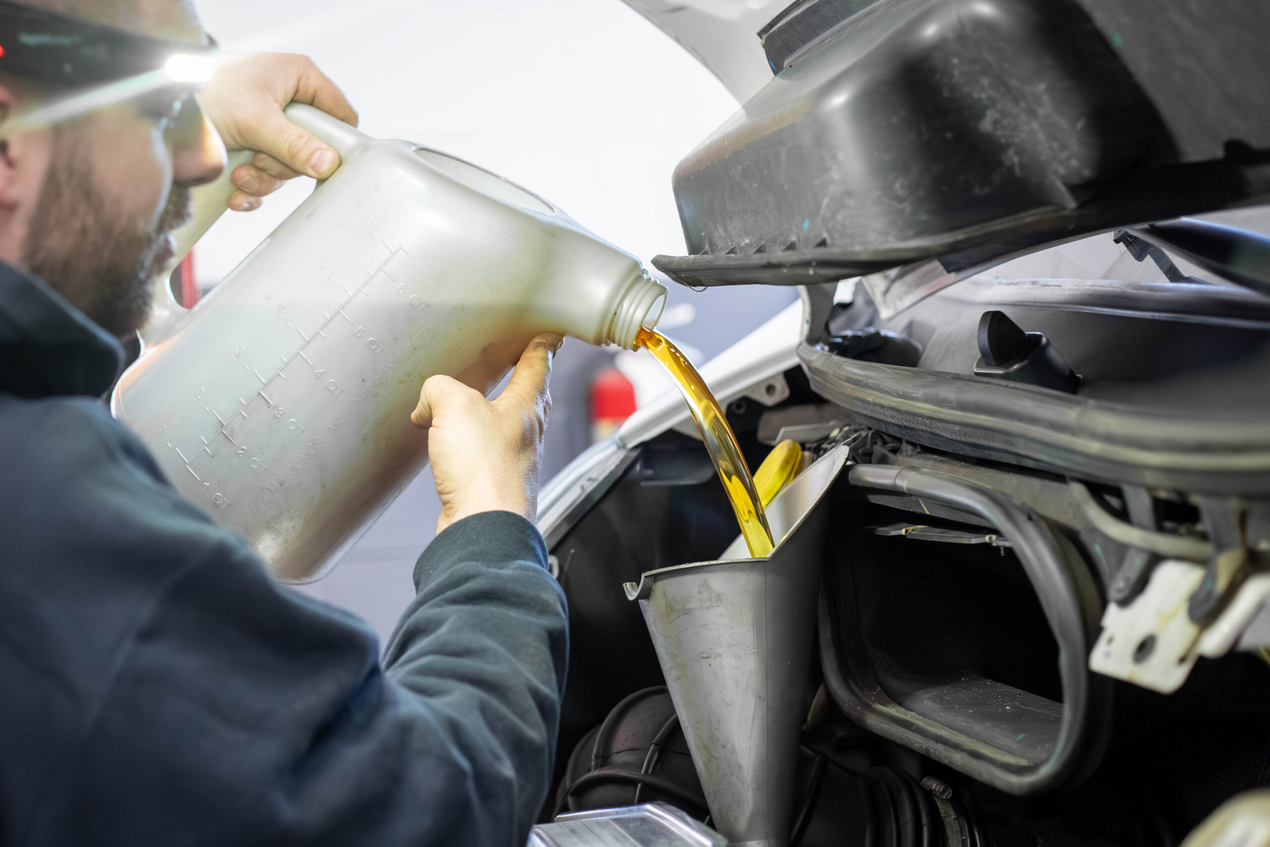 Close Up Of Tech Pouring Oil Into Grey Funnel