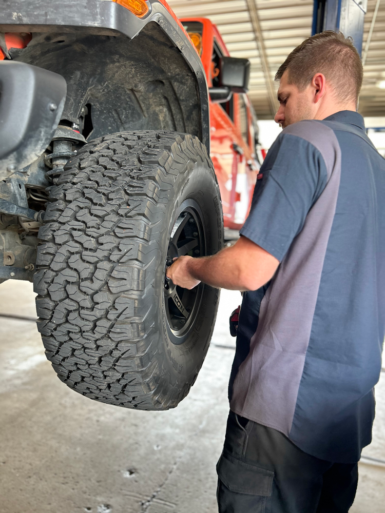 Preparing Your Car For Winter Technician inspecting a tire on an orange Jeep lifted in the shop.