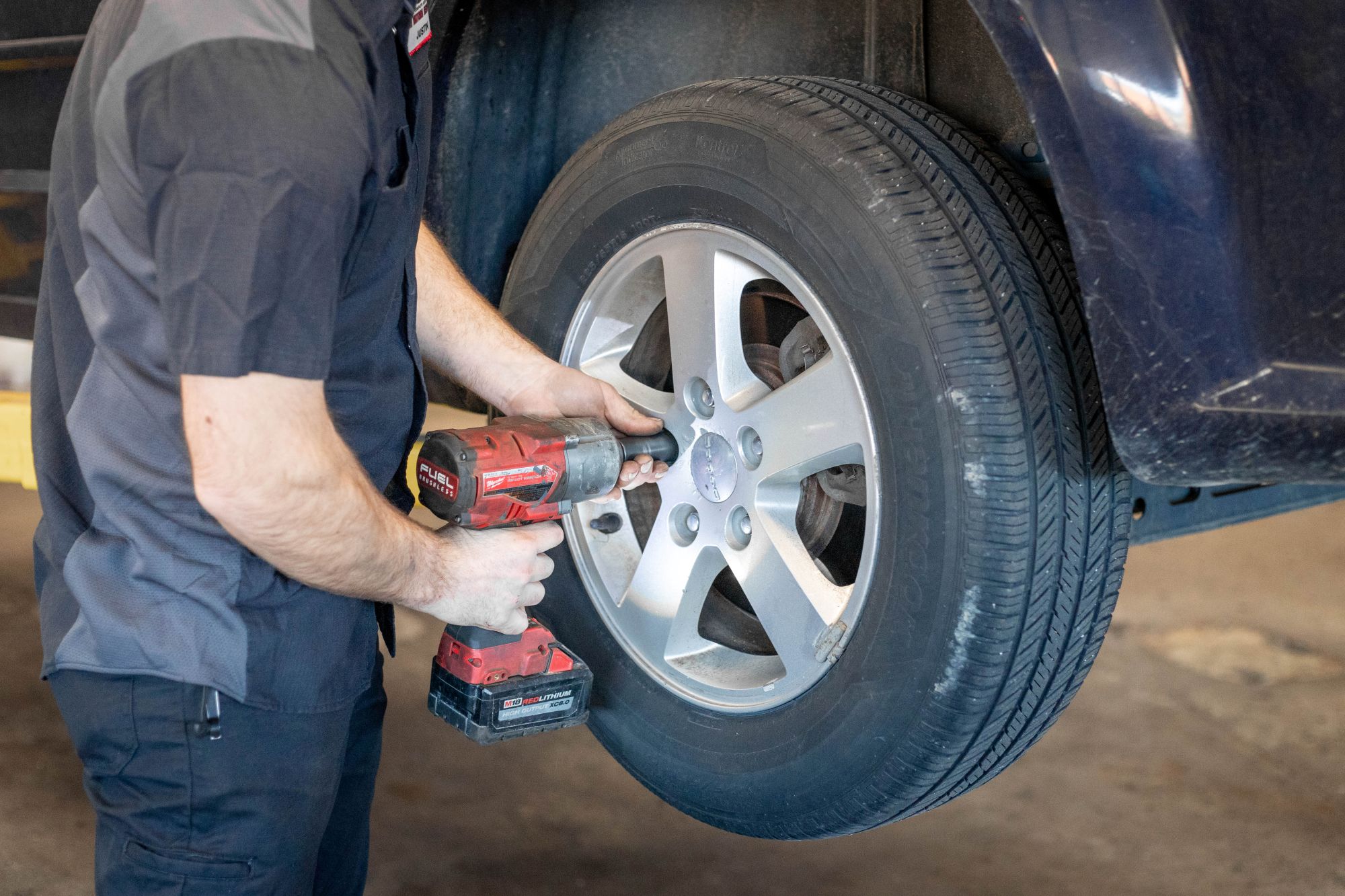 Side Angle Of Tech Screwing In Lug Nuts In A Tire - Web